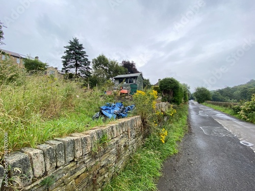 Back country road, with stone walls, a green hut, and plants on a rainy day, in Meltham, Huddersfield, UK