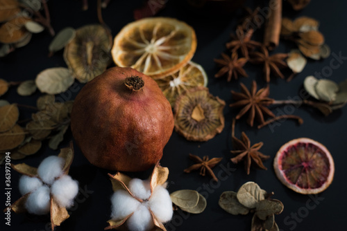 Dried pomegranate on black background with cold light. Autumn leaves, cinnamon, cotton flowers, slices of dry lemon, mandarin, kiwi and anis