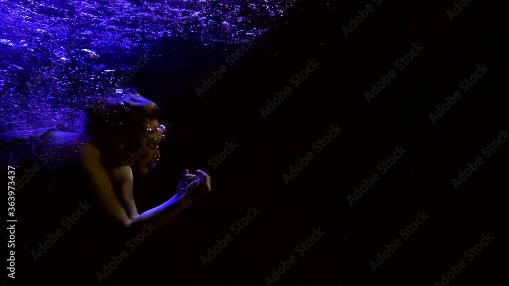 Close-up portrait of a girl who swims beautifully under water on a black background, wearing a corset, a long flowing skirt. On the surface of the water, its reflection, bubbles around it. Close-up portrait of a girl who swims beautifully under water on a black background, wearing a corset, a long flowing skirt. On the surface of the water, its reflection, bubbles around it.
