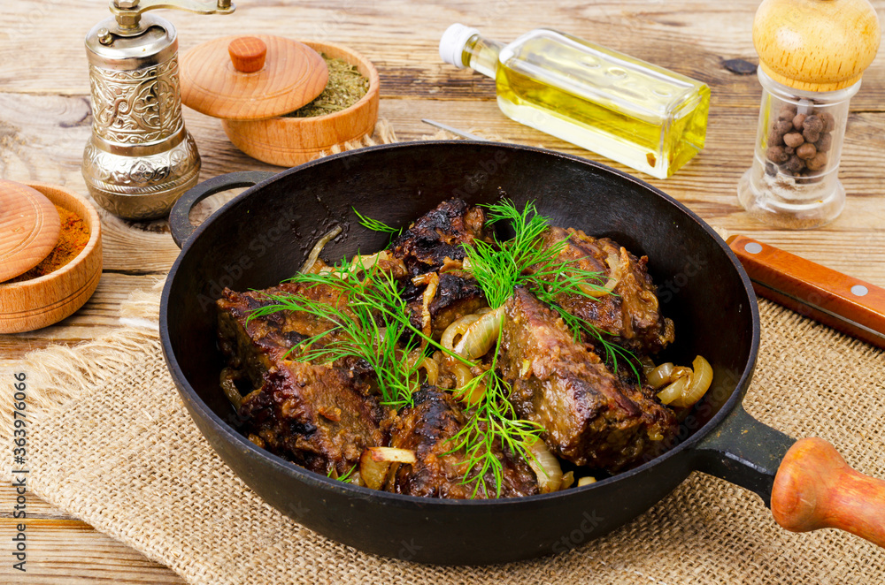 Cast-iron frying pan on wooden table with fried liver.