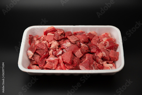 Raw diced meat (chopped in cubes) in a white styrofoam container isolated on black background copy space