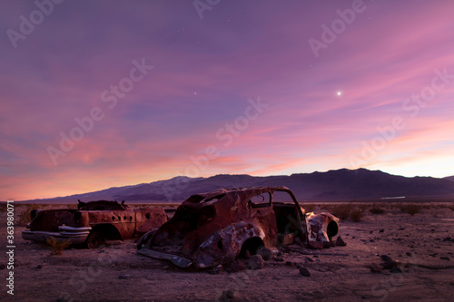 The sun sets in the Panamint Valley in Death Valley National Park in California. Rusted and abandoned old cars are seen in the foreground. The Argus mountain range is seen in the background.