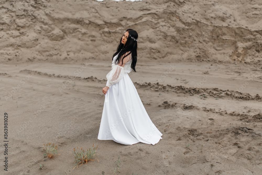 beautiful pensive girl in a white puffy dress and a wreath on her head is walking along a sandy quarry beautiful pensive girl in a white puffy dress and a wreath on her head is walking along a sandy quarry