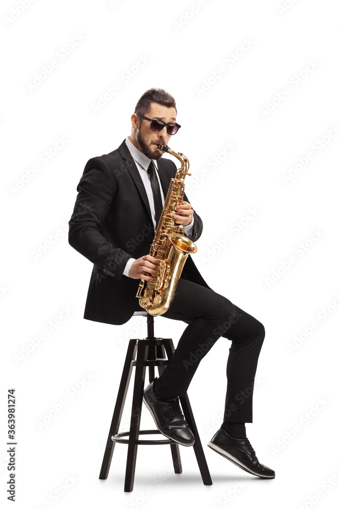 Fototapeta premium Elegant musician in a black suit playing a saxophone and sitting on a chair