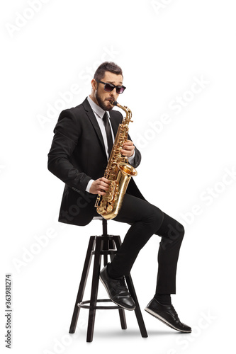 Elegant musician in a black suit playing a saxophone and sitting on a chair