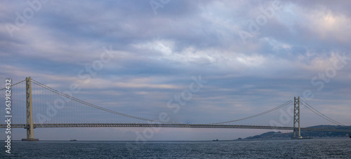 Panoramic view of long suspension bridge under beautiful clouds after sunset © Osaze
