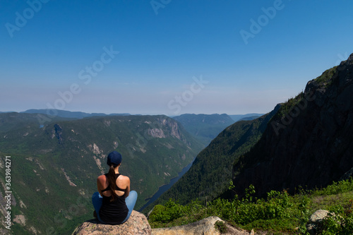 Young woman standing on the edge of a cliff at the summit of a mountain in the Hautes-gorges-de-la-rivière-Malbaie national park, Canada 