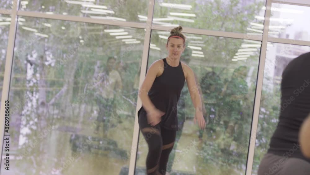 Live camera, positive woman showing movement in gym. Portrait of female Caucasian fitness instructor training people in sports club. Active young sportswoman at workplace. Live camera, positive woman showing movement in gym. Portrait of female Caucasian fitness instructor training people in sports club. Active young sportswoman at workplace.