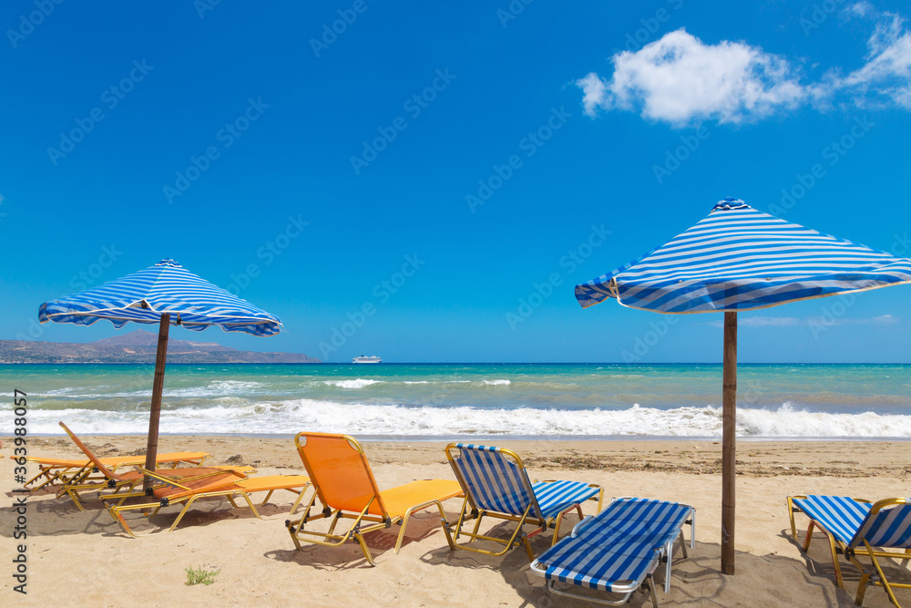 Crete beach Kalyves. Blue and yellow umbrellas and sunbeds against the backdrop of a beautiful blue sea on a sunny day. Public beach Kalyves in Crete Island in Greece