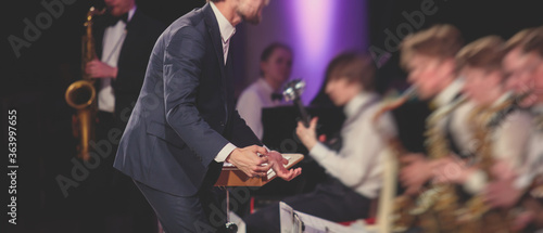 Canvas Print Young male Conductor directing symphony orchestra with performers in the backgro