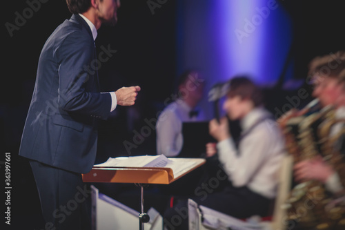 Photography Young male Conductor directing symphony orchestra with performers in the backgro