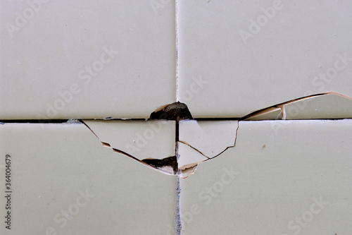 Cracked, broken bathroom wall tiles or panels - closeup view. © Sweeann
