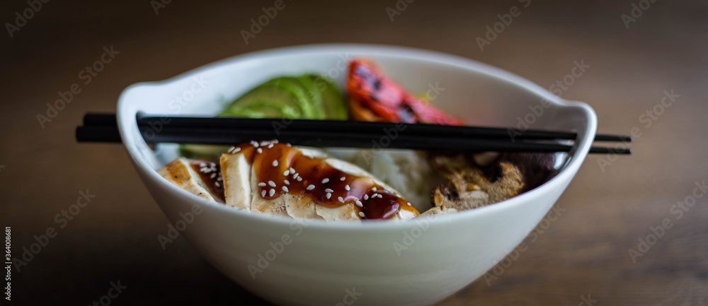 Asian rice bowl with grilled chicken breast, avocado, portobello mushrooms and peppers. Chopsticks on the top of the bowl Asian rice bowl with grilled chicken breast, avocado, portobello mushrooms and peppers. Chopsticks on the top of the bowl