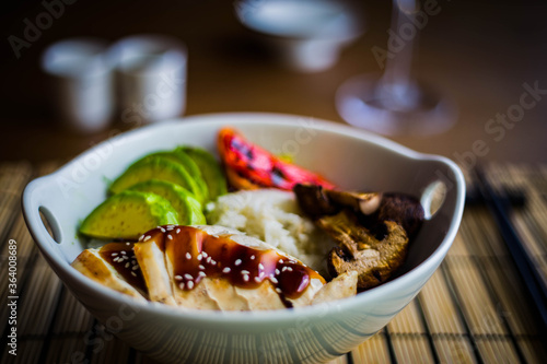 Asian rice bowl with grilled chicken breast, avocado, portobello mushrooms and peppers. Chopsticks on the background.