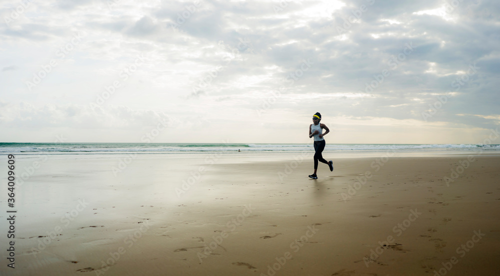 wide lens silhouette of afro American runner woman jogging on the beach - young attractive and athletic black girl training outdoors doing running workout at the sea wide lens silhouette of afro American runner woman jogging on the beach - young attractive and athletic black girl training outdoors doing running workout at the sea