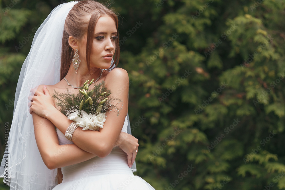 Beautiful bride in a magnificent wedding dress posing among greenery on the street. Bride concept for advertising dresses Beautiful bride in a magnificent wedding dress posing among greenery on the street. Bride concept for advertising dresses