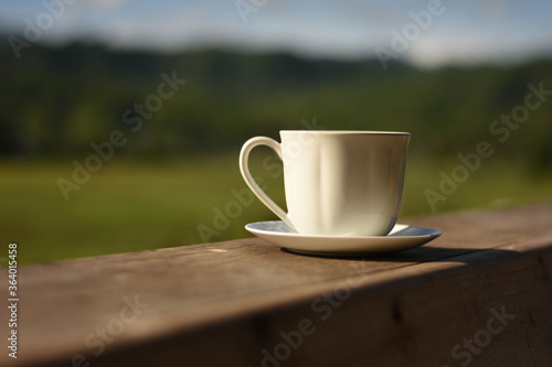white cup of coffee on wooden table,blur background,sunlight.
