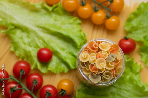 Pasta with vegetables in a plate. Ingredients for cooking tomatoes, cherry greens. With basil. Background from spaghetti. On the table, top view. 