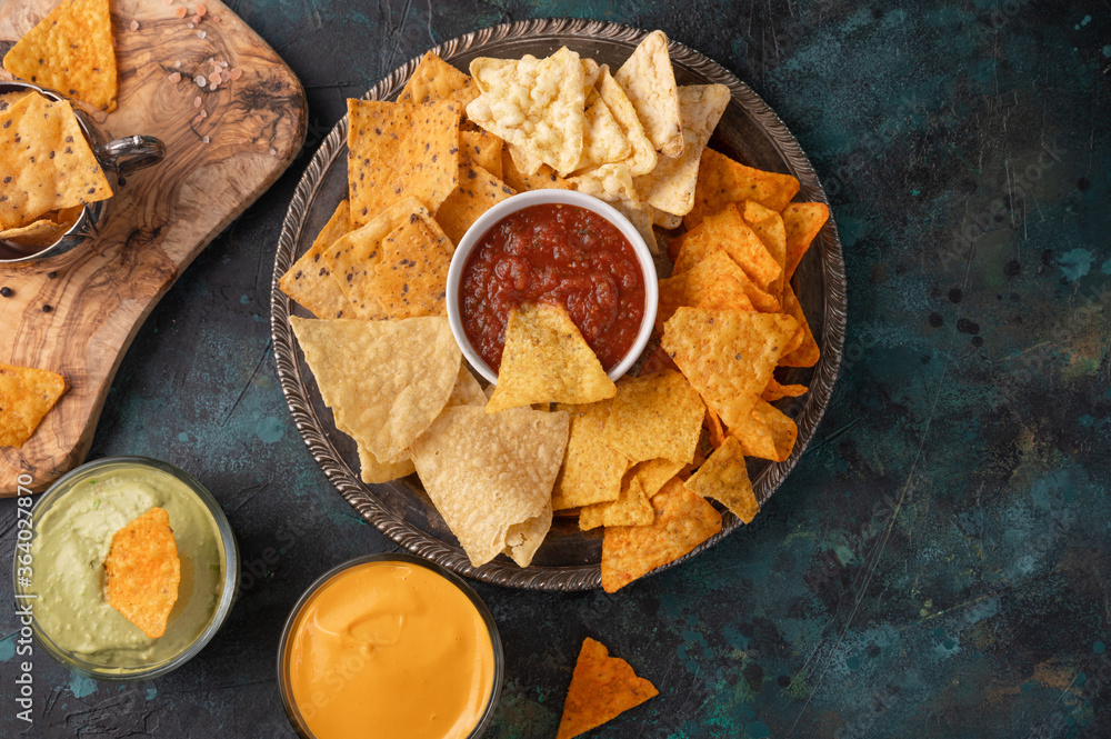 A plate of various snacks, potato chips, pita chips served with cheese, avocado, rosemary, and salt dip on a blue background. View from above. Copy space A plate of various snacks, potato chips, pita chips served with cheese, avocado, rosemary, and salt dip on a blue background. View from above. Copy space