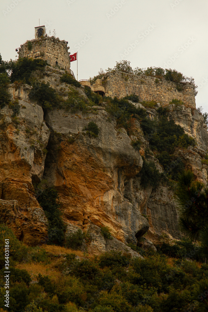 Image of the iconic Castle of Gozne on top of steep cliffs. The castle is located on top of Taurus mountains in Mersin Province of Turkey. A Turkish flag and a picture of Ataturk is seen on the walls.