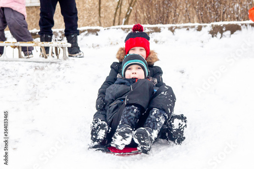 A boy rides from a snow slide on a red cardboard. Fun games in the snow. Two friends are lying in the snow. Snowy winter in Russia.