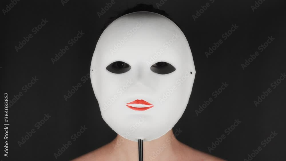 Brunette puts on a white theater mask. Theatrical makeup sad mask. Girl hides emotions behind a mask. Brunette puts on a white theater mask. Theatrical makeup sad mask. Girl hides emotions behind a mask.