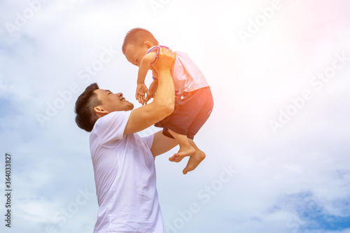 The father and the child are playing together under the blue sky and white clouds