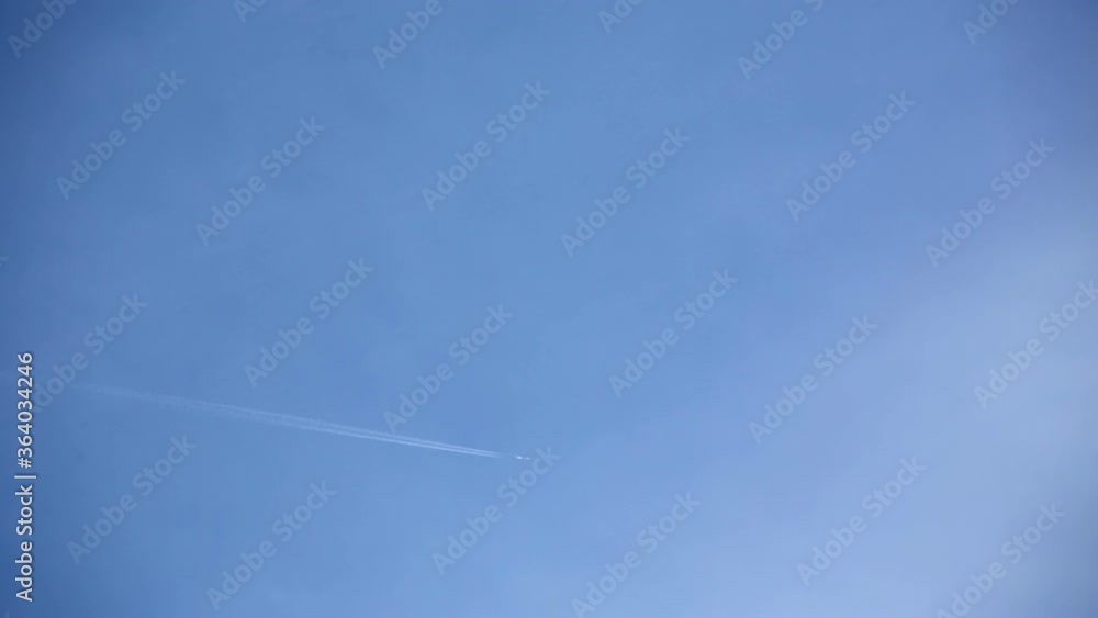 Airplane flying through the white clouds in blue sky. Chemtrails spreading behind aircraft Airplane flying through the white clouds in blue sky. Chemtrails spreading behind aircraft