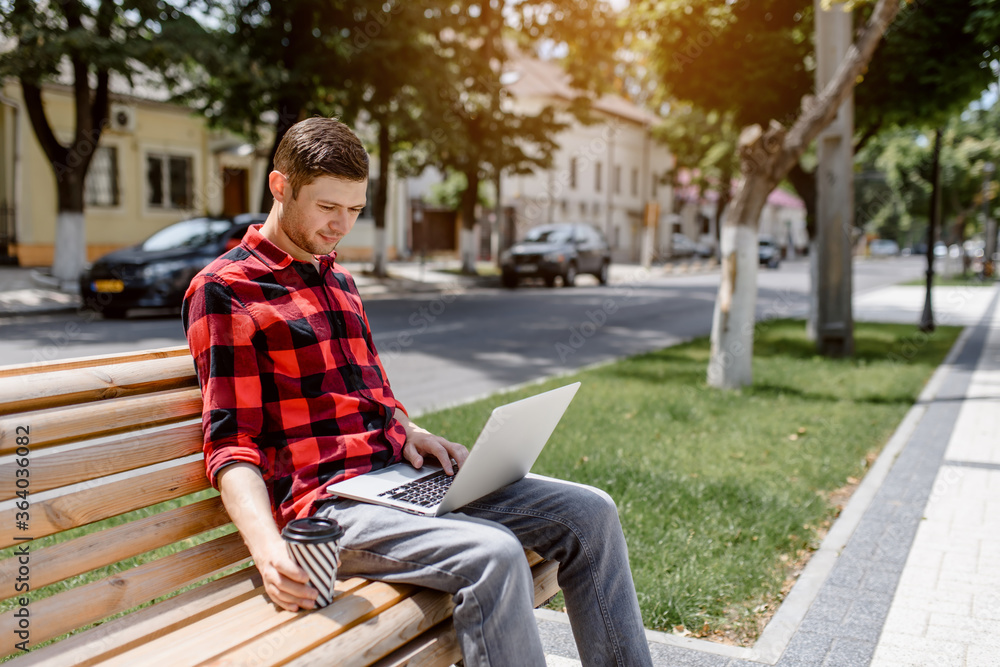 Happy young man freelancer is working outdoors on his computer laptop