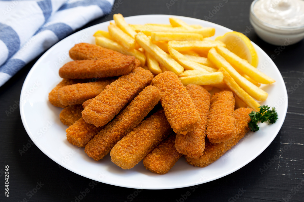 Homemade Fish Sticks and Fries with Tartar Sauce on a black surface, side view. Close-up. Homemade Fish Sticks and Fries with Tartar Sauce on a black surface, side view. Close-up.