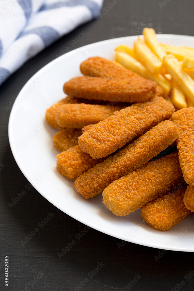 Homemade Fish Sticks and Fries on a white plate on a black background, side view. Close-up. Homemade Fish Sticks and Fries on a white plate on a black background, side view. Close-up.