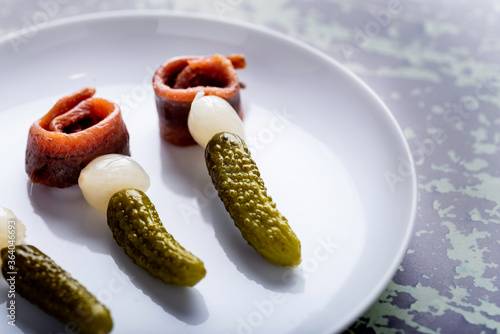 anchovy onion and gherkin skewers on a plate surrounded by ingredients