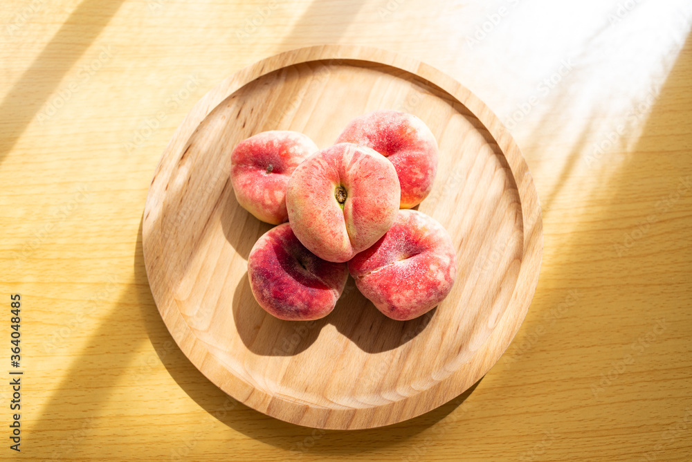 A plate of fresh flat peaches on a wooden table