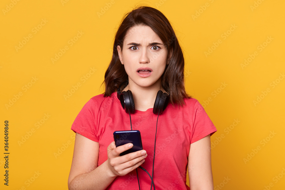 Portrait of astonished girl use cellphone for reading social media notification, being impressed and shocked, wearing casual clothes isolated, looks astonished. Portrait of astonished girl use cellphone for reading social media notification, being impressed and shocked, wearing casual clothes isolated, looks astonished.