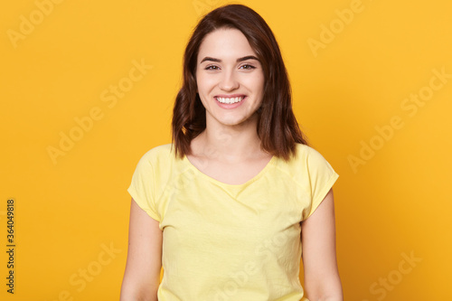 Young laughing woman against yellow background, brunette lady wearing casual attire posing with toothy smile, having good news, being in good mood, expressing happiness.
