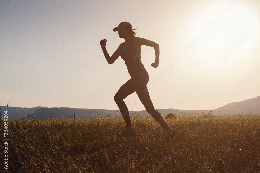 Jogging woman running in summer field at sunset