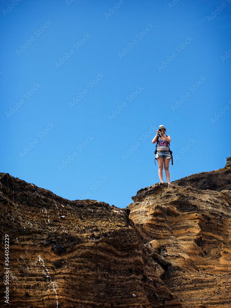 Chica joven haciendo fotos en la cima  de una montaña con el cielo azul de fondo