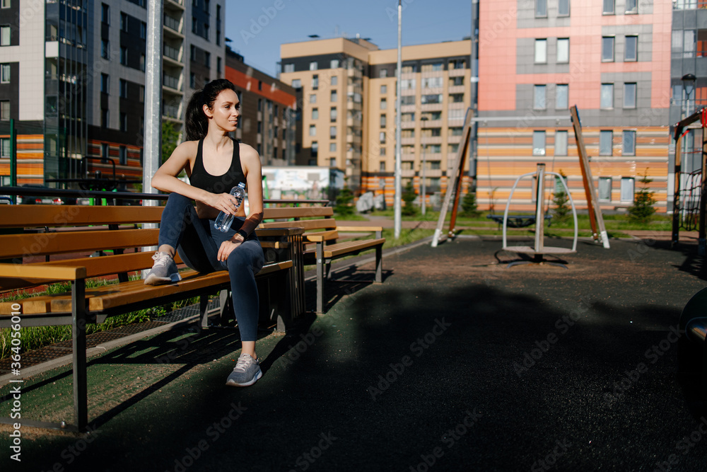 Beautiful sporty woman drinking water while resting from exercise. Beautiful female runner standing outdoors drinking water from her bottle. Fitness woman taking a break after running workout.