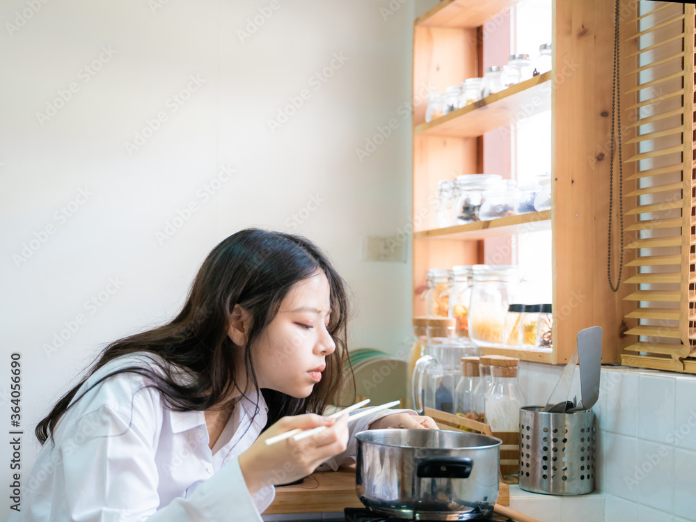 Beautiful asian casual girl is tasting food and smiling while cooking in kitchen Beautiful asian casual girl is tasting food and smiling while cooking in kitchen