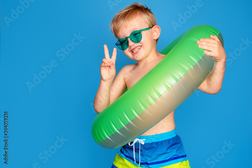Happy cute baby boy 6-7 years old in sunglasses and with a life buoy. Summer and the sea.