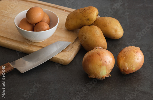 potatoes, eggs, onions, cutting table. knife on dark background