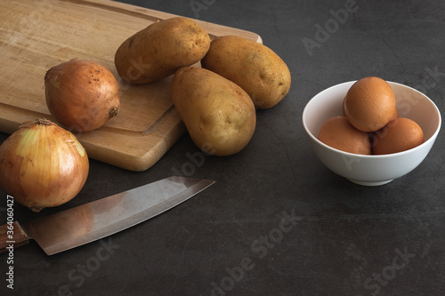potatoes, eggs, onions, cutting table. knife on dark background