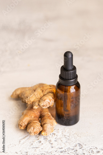 Essential ginger oil in glass bottle and ginger root on light concrete background. Concept for alternative health care and wellness