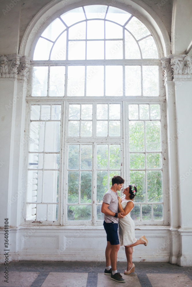 Fototapeta premium A beautiful couple strolling through the Park. Husband and wife walking in a beautiful Park. The architecture is white. A woman in a white dress on a date. Romance. First love. Tenderness.
