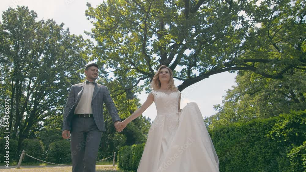 Young wedding couple in love newlyweds walking in a fabulous sunny park on a background of green trees. Brides walk in the park on a sunny day. Young wedding couple in love newlyweds walking in a fabulous sunny park on a background of green trees. Brides walk in the park on a sunny day.