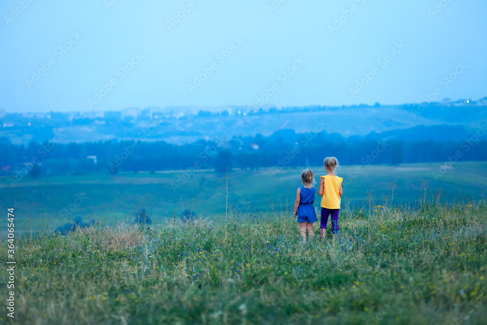 Two children in the summer stand in a field on a hill and look into the distance. Future vision concept. Walks in the open air. Family, little sisters walk and play together