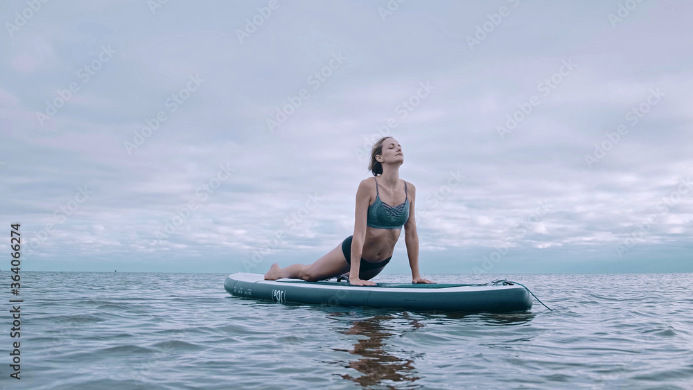 woman performs exercises from yoga on a surfboard. Yoga surf workout