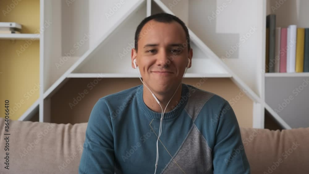 Calm happy young man in headphones chilling sitting on sofa listening to favorite music. Mood wearing earphones at home Calm happy young man in headphones chilling sitting on sofa listening to favorite music. Mood wearing earphones at home