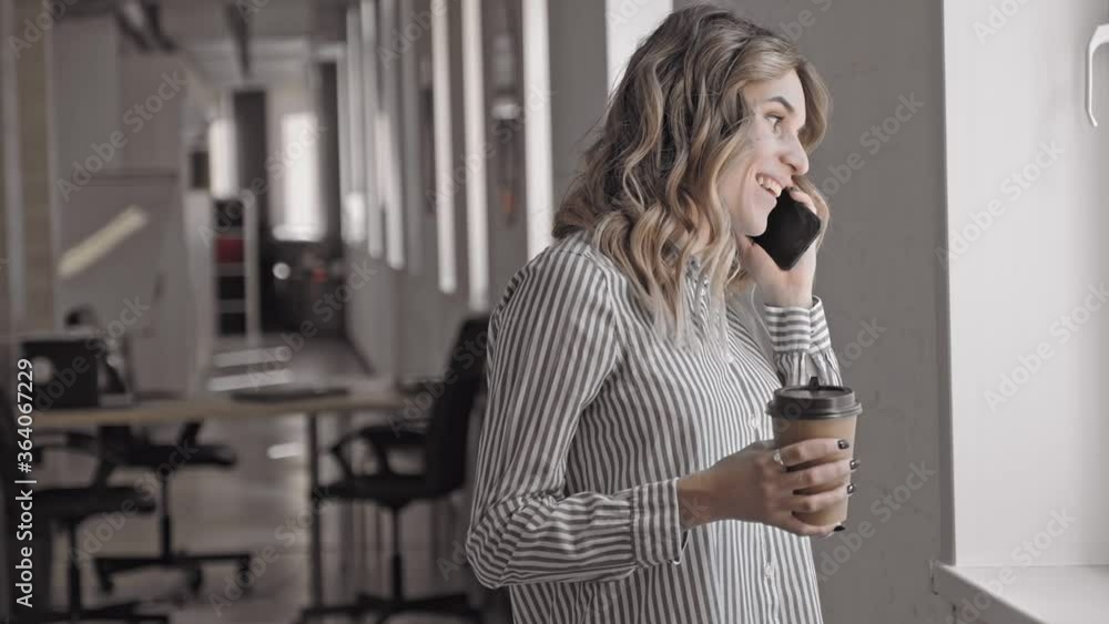Smiling professional woman making a friendly phone call, could be talking to a business contact or a friend. Irrl Slow motion during coffee break. holding tea paper cup Smiling professional woman making a friendly phone call, could be talking to a business contact or a friend. Irrl Slow motion during coffee break. holding tea paper cup