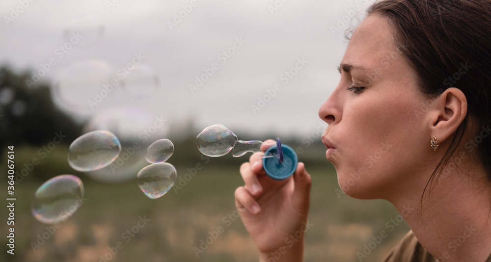 The girl blows soap bubbles. A young woman sits in nature and blows soap balls. Face in profile. The girl blows soap bubbles. A young woman sits in nature and blows soap balls. Face in profile.